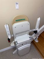 Angled view of folded beige vinyl seat, armrests and rail attached to stairs