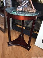 Full view of triangular green stone top corner table with three slender wooden legs and a triangular wooden base.