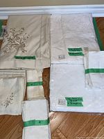 Full view of assorted table linens including tablecloths and napkins bundled with green tape and labeled sizes.
