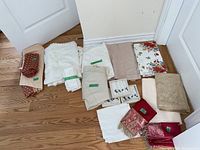 Full lot overview showing folded linens, including tablecloths, runners, and napkins in cream, white, beige, brown, red and floral patterns