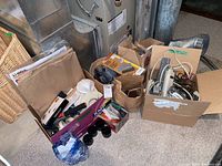 Boxes containing various tools, cords, hardware, and supplies arranged on basement floor