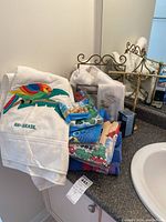 Photo of metal towel stand holding multiple towels including one white towel with colorful parrot and 'RIO-BRASIL' embroidery with assorted patterned towels beneath. Soap bar visible near towels.