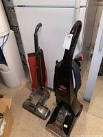 Two vacuum cleaners side by side: Bissell ProHeat carpet cleaner and Kirby upright vacuum.