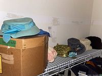 Several vintage hats placed on a wire rack shelf with a cardboard box labeled 'vintage hats' underneath. Hats include a pastel blue wool hat with ribbon bow, gold sequined hat, and a crocheted hat with pink stripes.