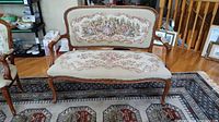 Full view of the vintage tapestry settee showing the carved wooden frame and floral upholstery on the seat and backrest.