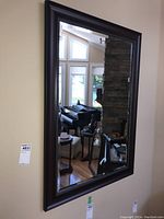 Full view of the rectangular wall mirror hanging on a wall in a room with hardwood floors, reflecting a grand piano and furniture.