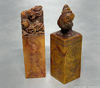 Front view of two Chinese Shoushan stone chop seals side by side on a grey surface, showing detailed carved tops and engraved sides.