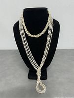 Front view of both freshwater pearl necklaces displayed on black bust stand. The longer necklace shows multi-strand pearls knotted in front and the shorter necklace shows a braided multi-strand design.