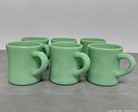 Front view showing six forest green ceramic mugs in two rows, arranged on a plain surface.