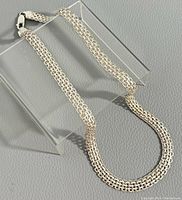 Full length view of necklace chain draped over clear acrylic stand showing link pattern and clasp