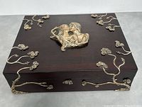 Front angled view of the wooden jewelry box showing the applied silver floral and vine motifs and the central silver relief of an embracing couple.