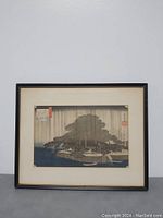 Framed artwork featuring a traditional Japanese rainy landscape scene with a large tree, water and structures visible. Art print is textured paper mounted under glass in a black frame.