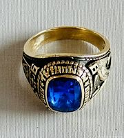 Top view of ring face showing square blue synthetic stone set in rope-style bezel and engraved wreath motif