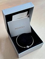 Open box showing the silver snowflake bangle on a black insert along with Pandora paperwork inside the box.