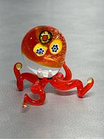 Front and side view of red glass octopus figurine featuring colorful embedded flower designs in the head and curled legs tipped with clear glass.