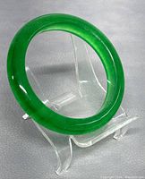 Natural jade bangle displayed on clear acrylic stand