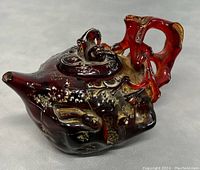 Side angle showing reddish-brown amber style teapot with carved lion lid and detailed handle.