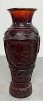 Front view of 12 inch tall amber pressed glass vase with intricate decorative Chinese-style relief patterns and flared rim.