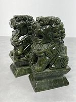 Pair of green stone Foo Dogs seated on tiered rectangular bases with detailed carving and polished finish