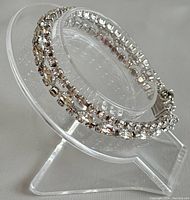 Side view of the bracelet on a clear stand showing the double row of clear rhinestones and silver-tone setting.