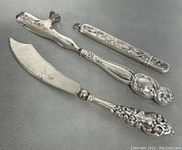 Three sterling silver handled tools including a nail file with cover, cuticle remover, and knife with ornate handles.