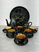Full display of the 12-piece black lacquer ware tea set with scenic mountain and nature paintings on tray, teapot, sugar pot, teacups, and saucers.