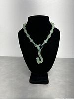 Full view of the vintage Chinese carved translucent opaque light green jade necklace displayed on a black stand showing length and pendant shape.