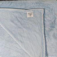 Calvin Klein label on powder blue plush blanket showing brand and care information.