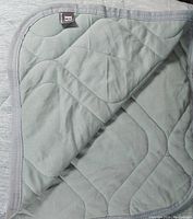 Photo showing corner of green cooling blanket with quilted pattern and gray binding.