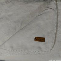 White plush blanket or throw folded to show the stitched edges and a corner with the Koolaburra fabric label sewn on.