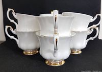 Eight white bone china teacups with gold accents arranged in a cluster showing handles and overall shape