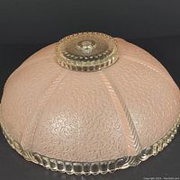 Side view of pink and white textured glass ceiling light shade with clear scalloped edge and ridged top hub.