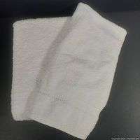 Two white towels laid out on a black surface in a folded arrangement showing texture and size difference.