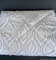 Full view of the folded blanket showing patterned top surface with a repeating symmetrical teardrop motif in neutral tones.