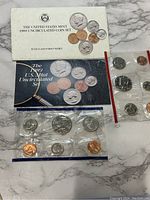 Photo showing the 1989 United States Mint outer white envelope with seal, black informational card, and two sealed uncirculated coin sets with visible pennies, nickels, dimes, quarters, and half dollars.