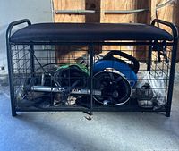 Front view of the storage cage bench showing the padded seat and interior contents including power tools.