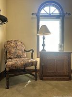 Vintage floral armchair placed next to the wooden White Clad icebox cabinet with lamp and clock on top.