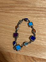 Front view of the bracelet showing various stone inlays in different shapes and colors on a wooden surface.