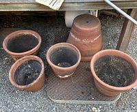Five vintage terra cotta planter pots placed on ground, showing various sizes and surface wear.