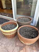 Three terra cotta planters filled with soil, placed outdoors on a tile surface near glass doors