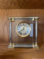 Front view of vintage Danbury glass mantel clock showing round dial with Roman numerals and gold bezel with gold and silver-tone columns on glass case