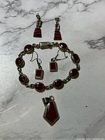 Photo showing all jewelry items: clip-on earrings, dangle earrings, bracelet, and pendant with red jasper set in silver.