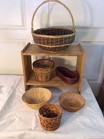 Small wooden shelf with six assorted wicker baskets placed on top and around it.