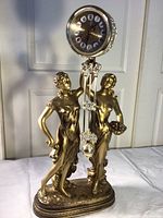 Front view of the gold-toned Grecian women clock sculpture with visible clock face