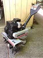 Side view of complete rototiller showing engine, tines, wheels, and handle assembly