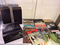 Photo showing the Fisher audio system components (turntable, cassette player, tuner) with two speakers and a spread of vintage vinyl record albums.