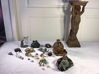 Group photo showing all various sized frog figurines and statues laid out on a white surface in front of a door.