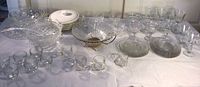 Wide view of entire collection of clear cut glass bowls, plates, stemware, punch cups, tumblers, and ceramic lidded dish in gold frame.