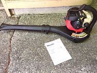Full view of Homelite Mighty Lite leaf blower on concrete with the original manual in front, showing the blower tube, handle, and fuel tank.