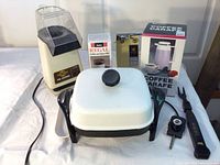Full view of all items including Presto electric skillet, Regal coffee grinder in box, coffee carafe in box, popcorn popper, and can opener on table.
